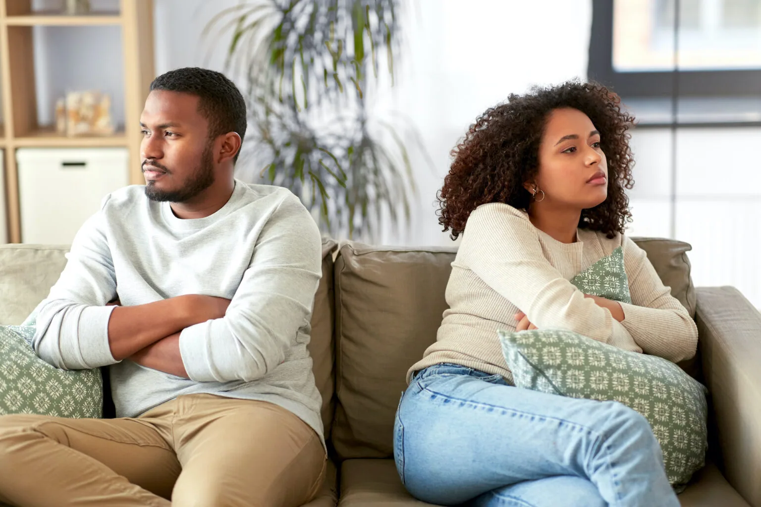 Two people sitting apart on a couch with arms crossed, appearing upset or distant from each other